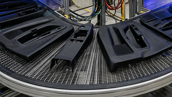 Automotive plastic trim parts on a conveyor belt passing through an inline plasma treatment station